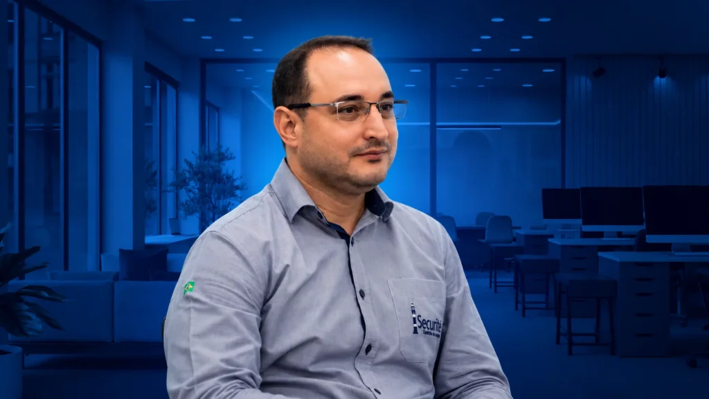 Homem com camisa da Securite em primeiro plano e escritório ao fundo em tons de azul.